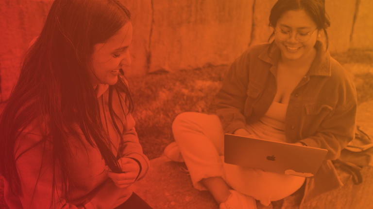 Two students chat while one uses laptop